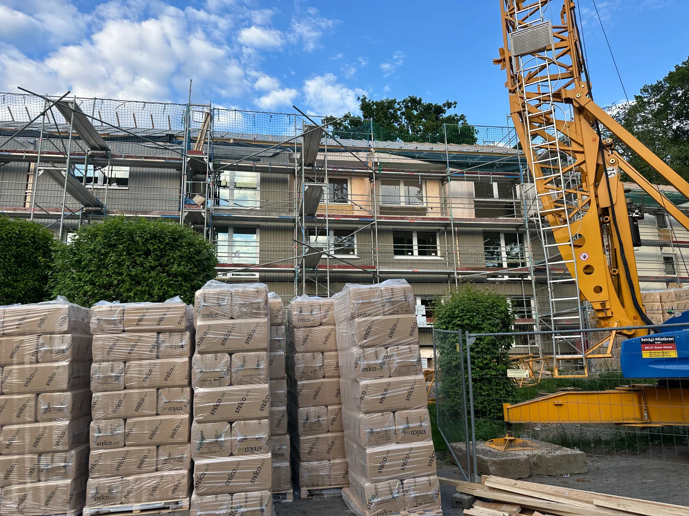 Serielles Fassadensanierungsprojekt im Gerüst: Kran und vorbereitete Materialpaletten am Gebäude
